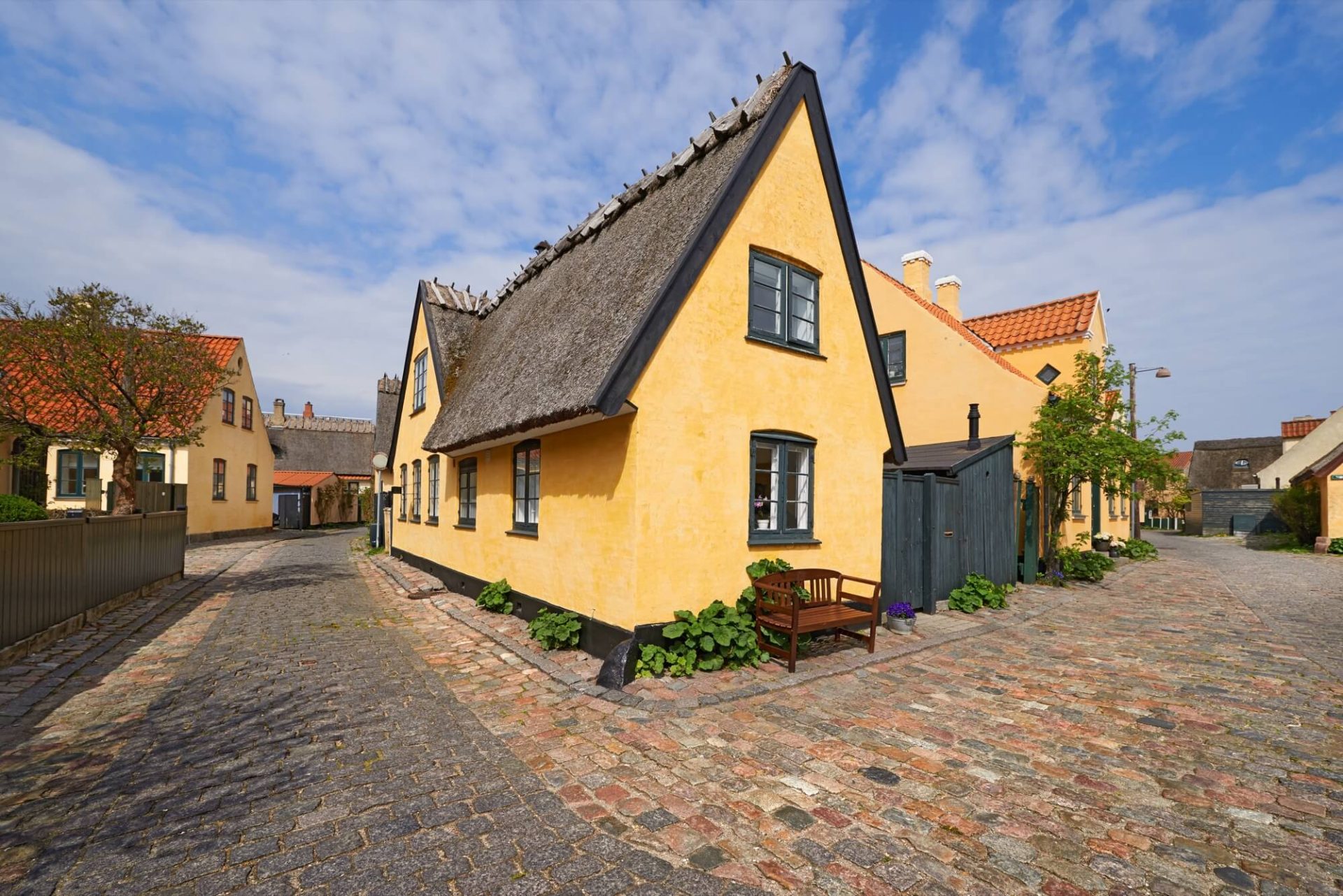 Huset på den pittoreska gatan har en charmig gammaldags exteriör med en gul putsad fasad, fönster i svart och ett tak av halm